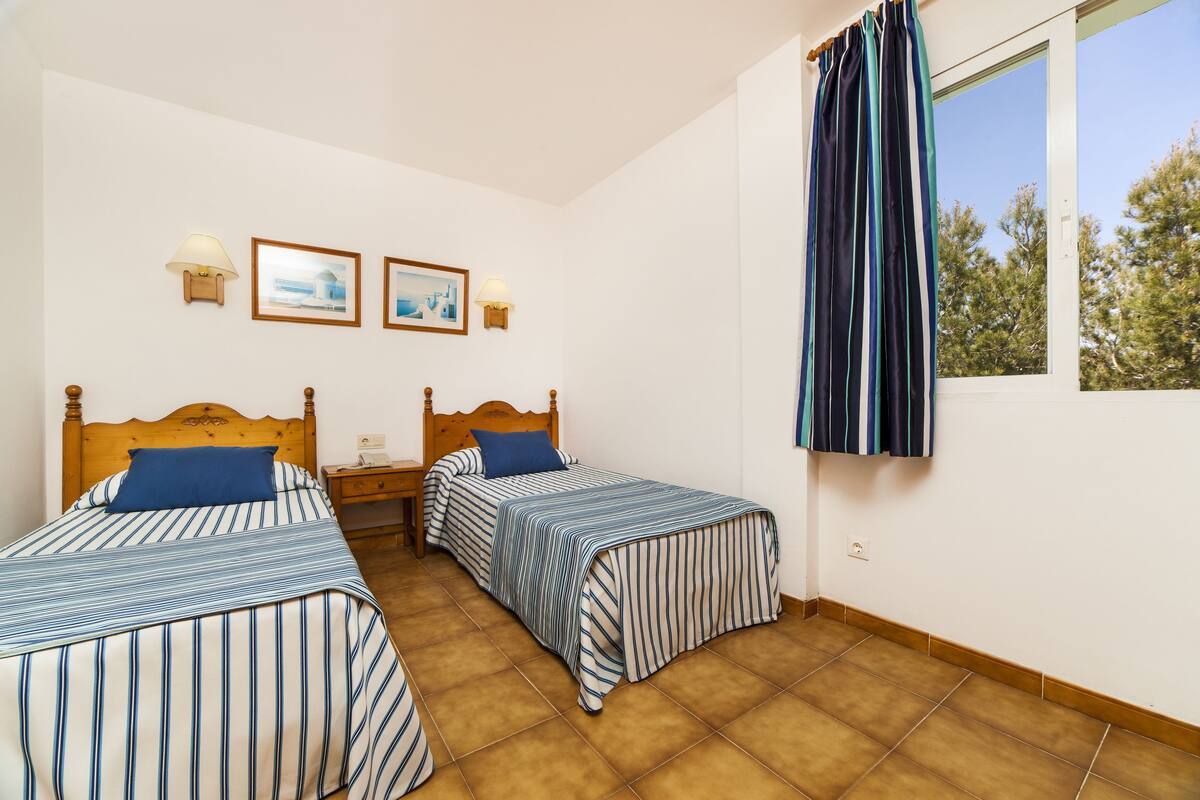 Ein Schlafzimmer mit zwei Betten, einem Fenster mit Vorhängen und Wandleuchten.