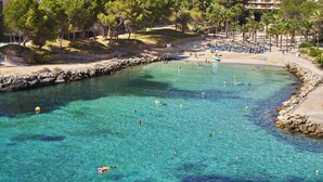 Un complejo turístico frente al mar, con aguas turquesas cristalinas, una playa arenosa y un litoral rocoso.