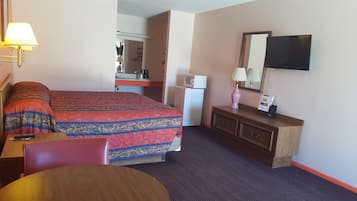 Ein Hotelzimmer mit Bett, Schreibtisch, Stuhl, Kommode, Mikrowelle, Kühlschrank, Lampe und Fernseher.