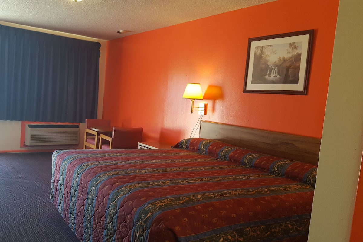 A hotel room with a large bed, a desk with a chair, a lamp, and a picture on the wall.