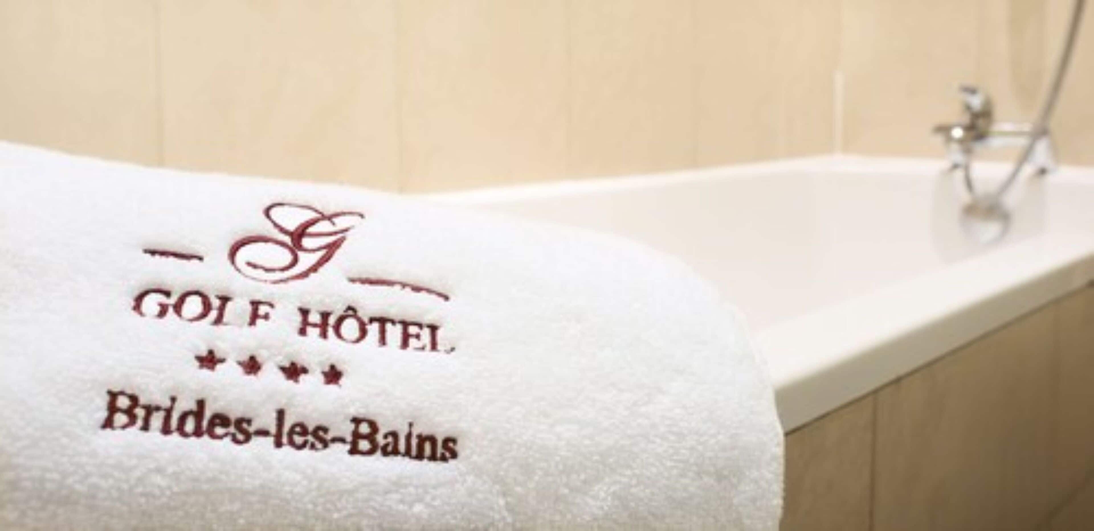 A white towel with embroidered text reading "GOLF HOTEL Brides-les-Bains" on a bathtub.