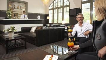 Un hall d’hôtel moderne doté d’un comptoir d’accueil, de sièges en cuir et d’une grande fenêtre laissant entrer la lumière naturelle.
