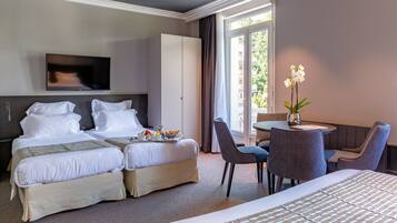 A hotel room with two beds, a TV, a dining table with chairs, and a window with curtains.