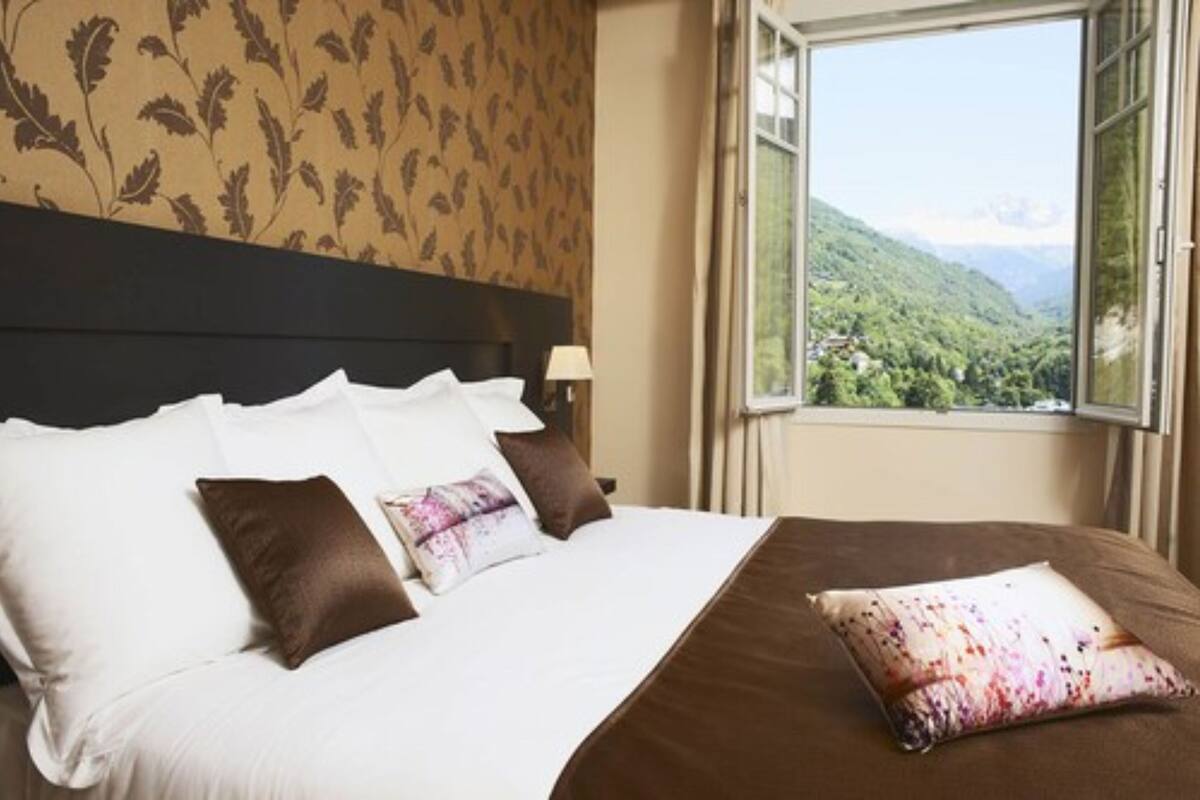Ein Hotelzimmer mit Bett, einem Fenster mit Blick auf eine grüne Landschaft und einer Wand mit Muster.
