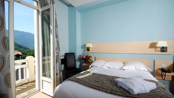 Habitación de hotel con cama, una silla, mesita de noche, lámpara, teléfono y vista a zonas verdes a través de una puerta corrediza.