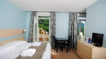 Habitación de hotel con cama, escritorio, televisor y vista a una casa por la ventana.