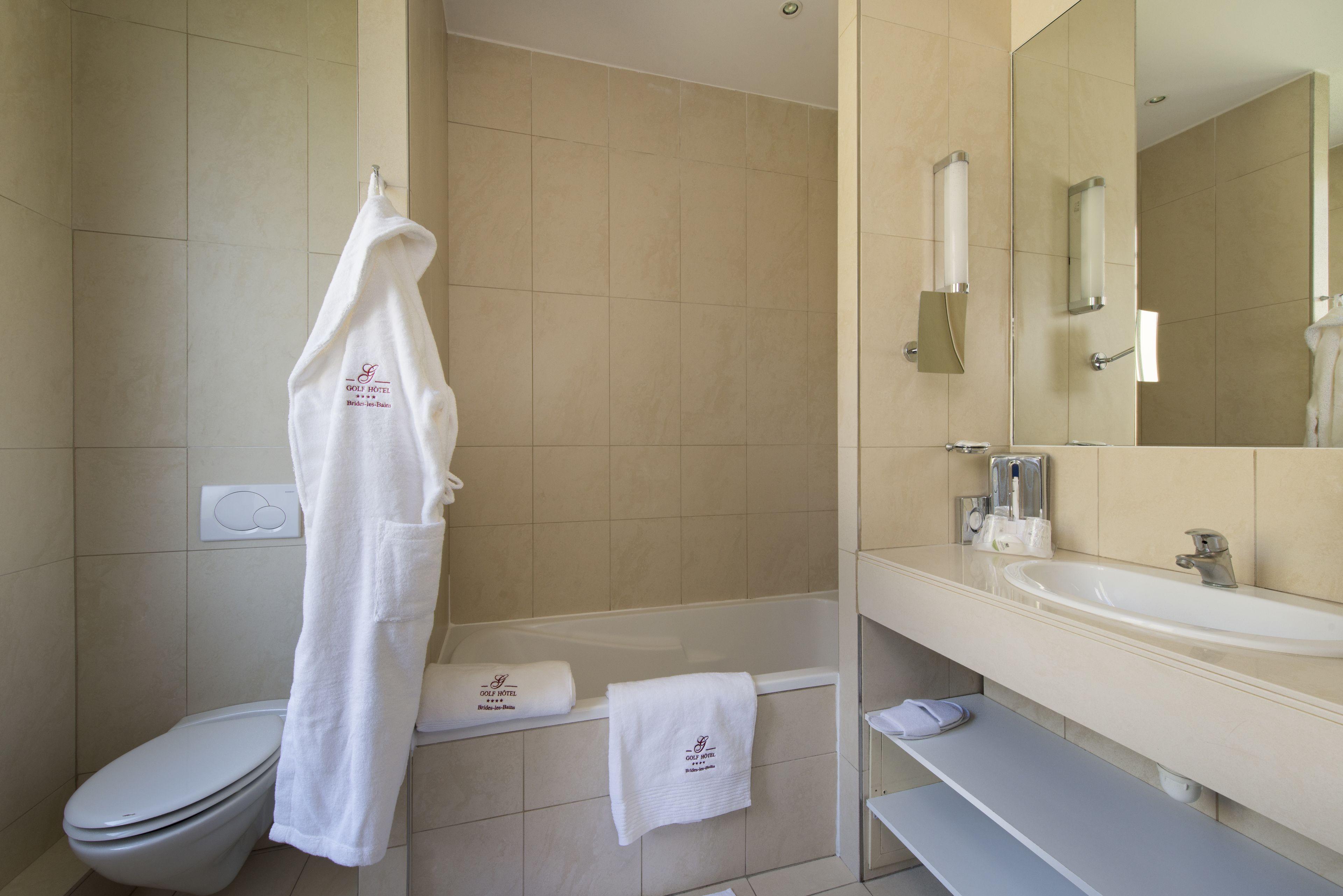 Un baño con inodoro, bañera y lavamanos. Hay toallas colgadas en la pared y un espejo sobre el lavamanos.