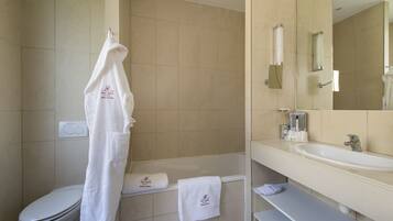 Un baño con inodoro, bañera y lavamanos. Hay toallas colgadas en la pared y un espejo sobre el lavamanos.