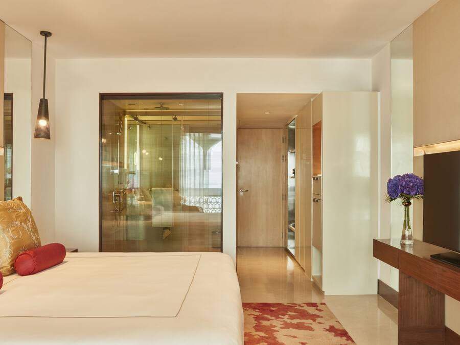 Quarto de hotel moderno com uma cama grande, uma televisão e banheiro com chuveiro de vidro.