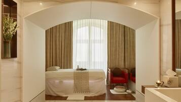 Relax in a serene space with a large bed, a small table, and a comfortable chair.