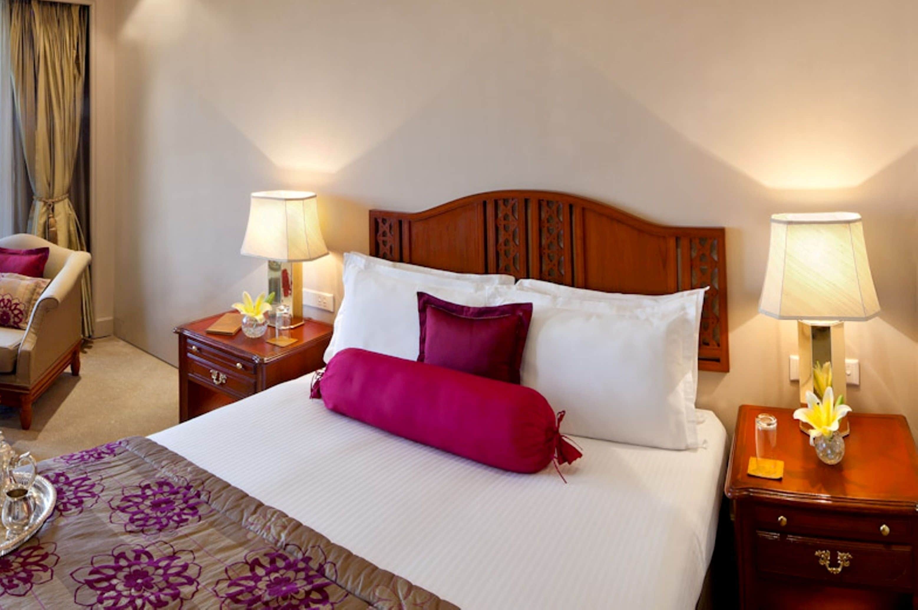 A hotel room with a large bed, two bedside tables, a chair, and a lamp on each side of the bed.