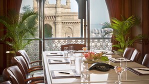 Une chambre d’hôtel dotée d’une grande fenêtre donnant sur un bâtiment historique. La chambre comprend une table à manger avec des chaises, un téléphone et un vase rempli de fleurs.