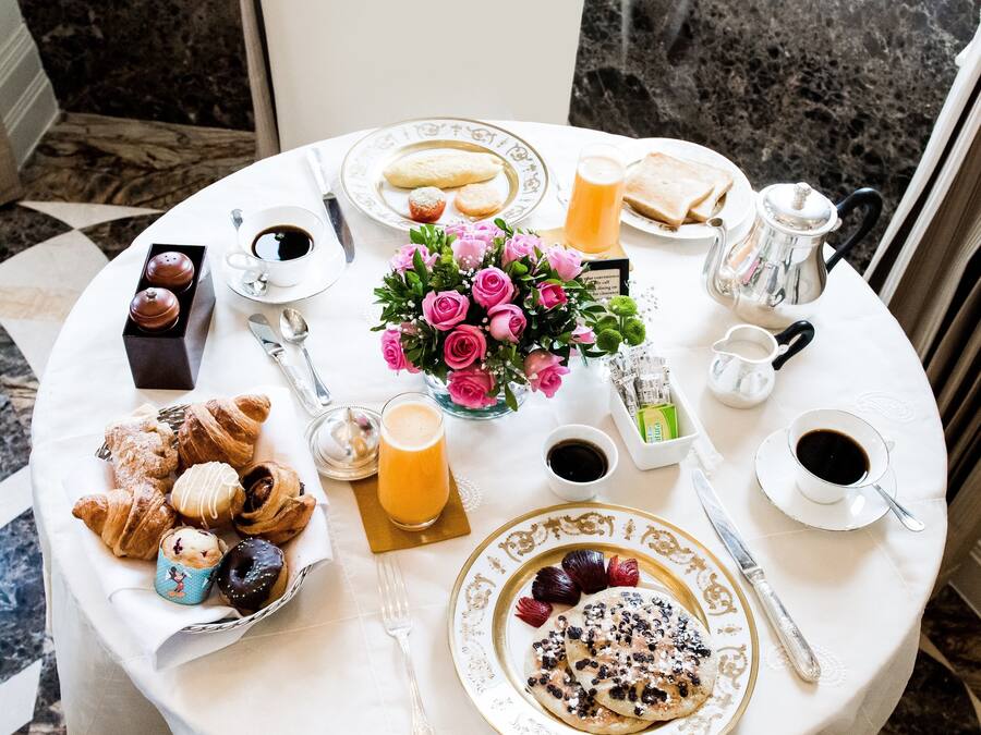 Una mesa de desayuno con pasteles, café, jugo y un ramo de flores.