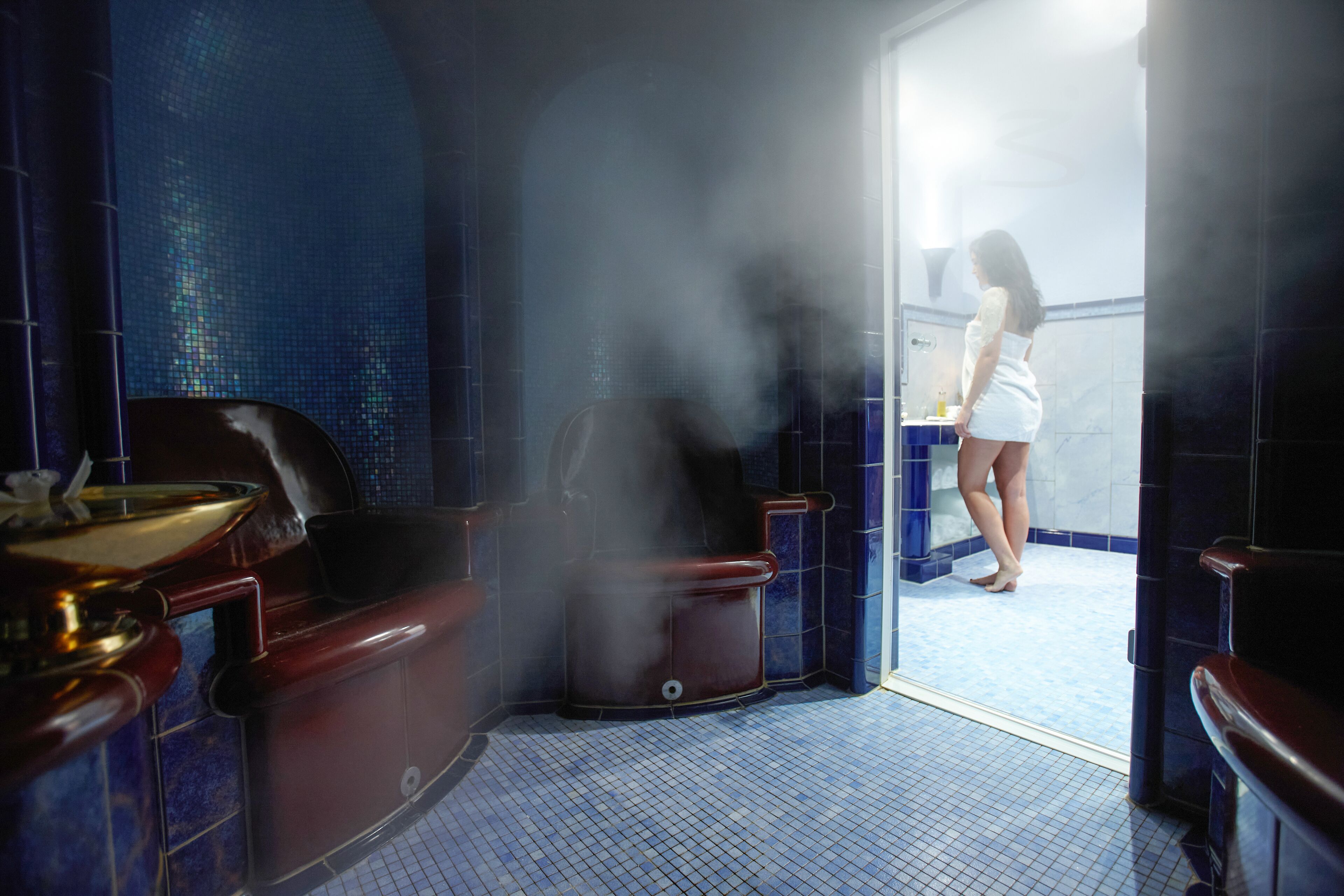 A steam room with a large tub, a small table with a bowl, and a tiled floor.