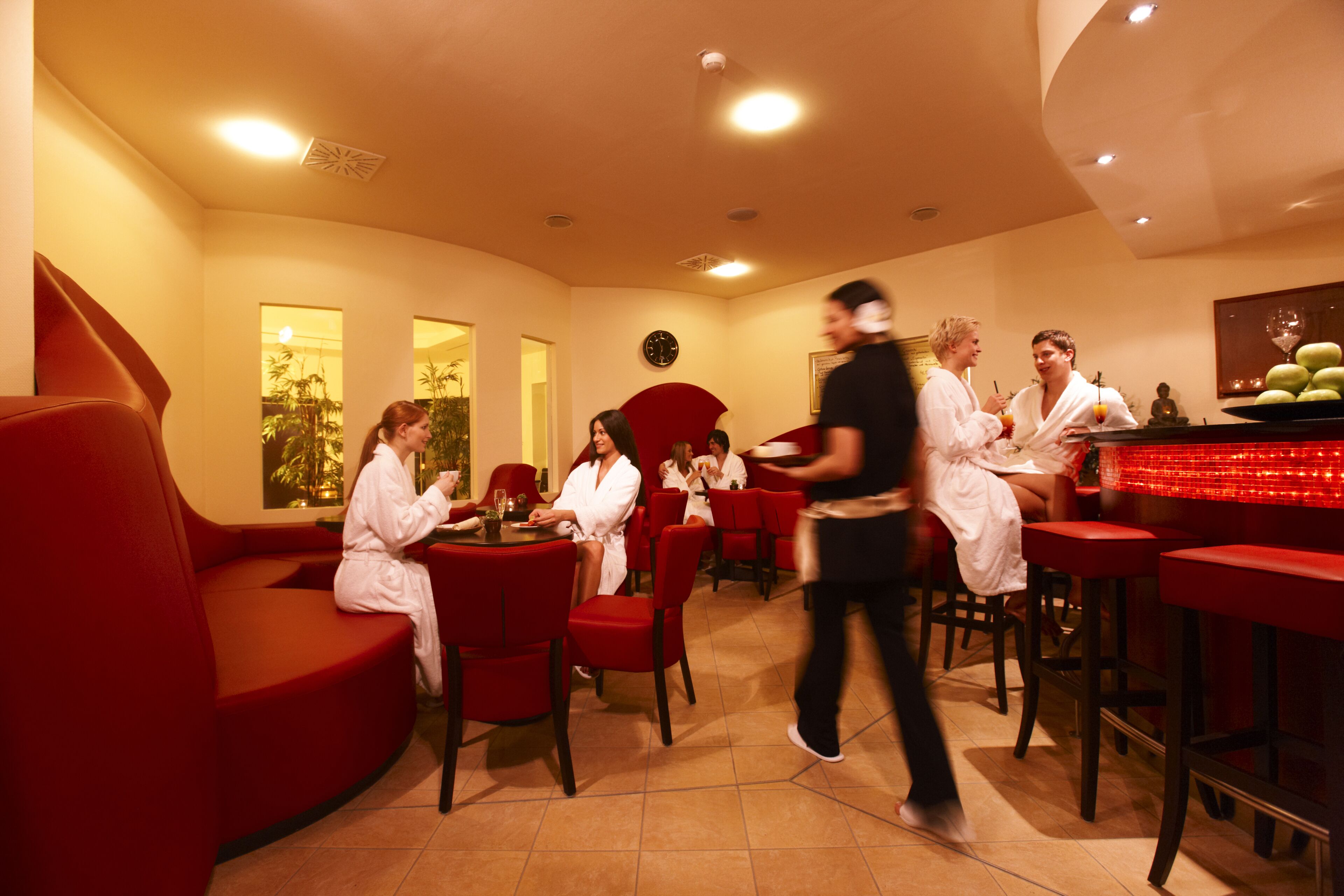 Un restaurante con sillas y mesas rojas, una zona de bar y un reloj en la pared.