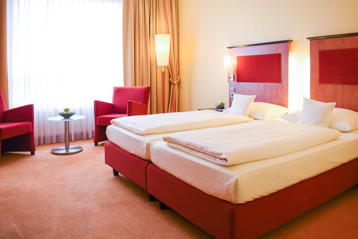 Une chambre d’hôtel avec deux lits, des chaises rouges, une petite table avec un bol et une lampe.