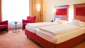 Une chambre d’hôtel avec deux lits, des chaises rouges, une petite table avec un bol et une lampe.