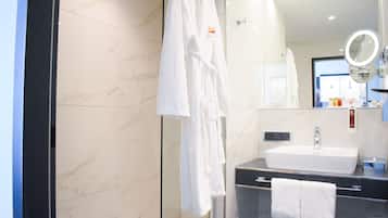 A modern bathroom with a marble wall, a white sink, a glass shower enclosure, and a robe hanging on a rack.