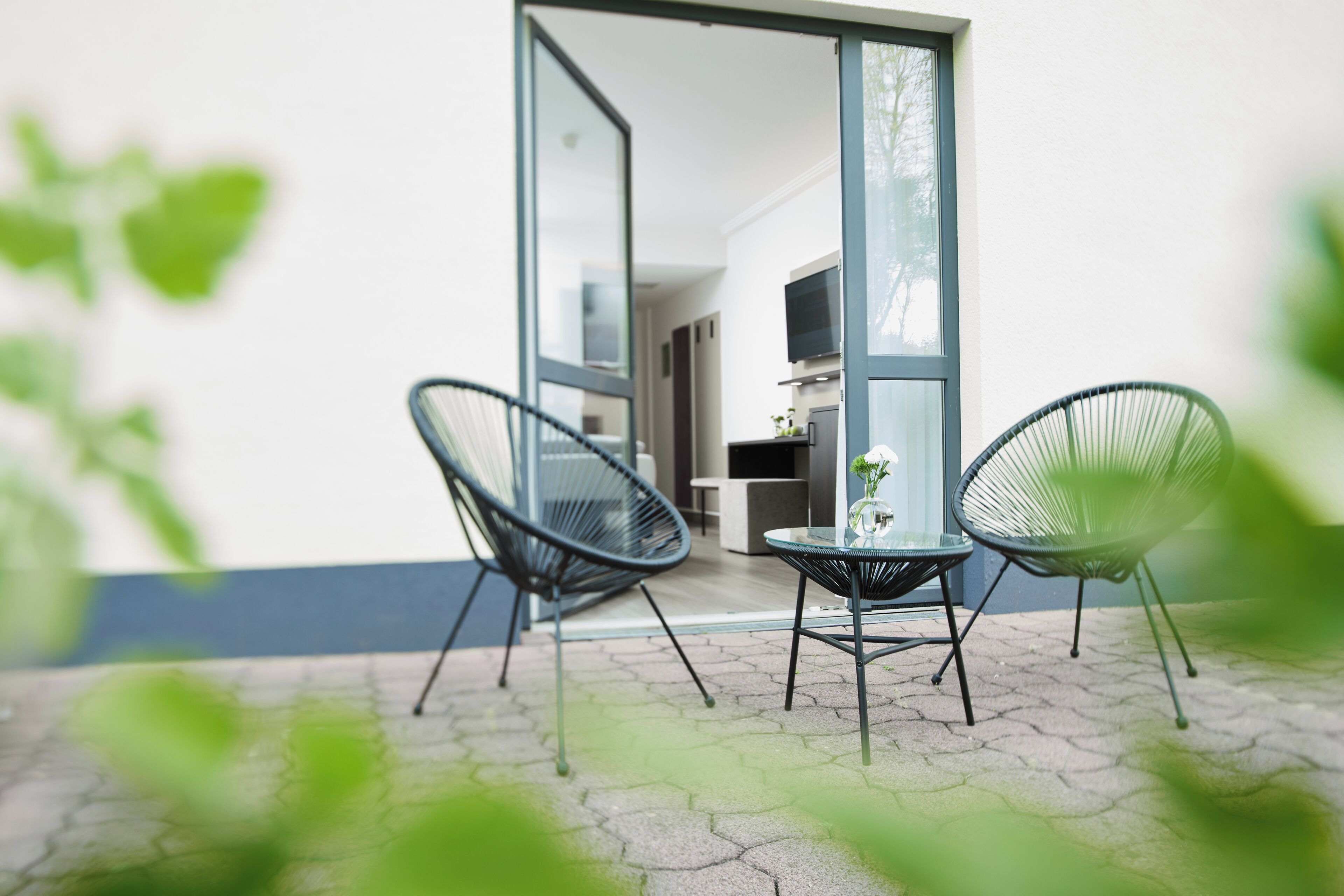 An outdoor patio with two chairs and a table, a glass door leading to an interior space, and a tiled floor.