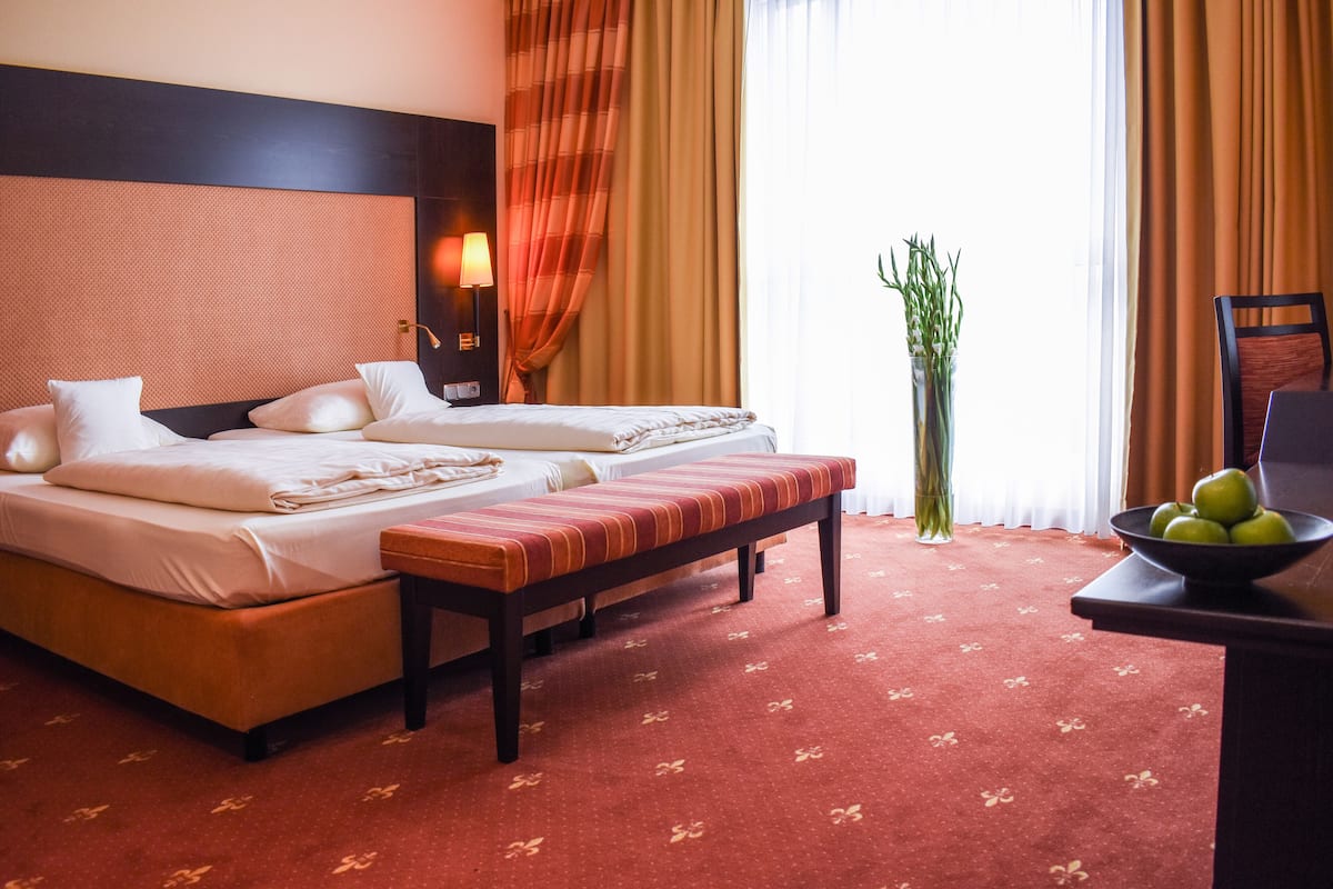Une chambre d’hôtel avec deux lits, un banc, une table de chevet sur laquelle se trouve un bol de fruits et une plante en pot.