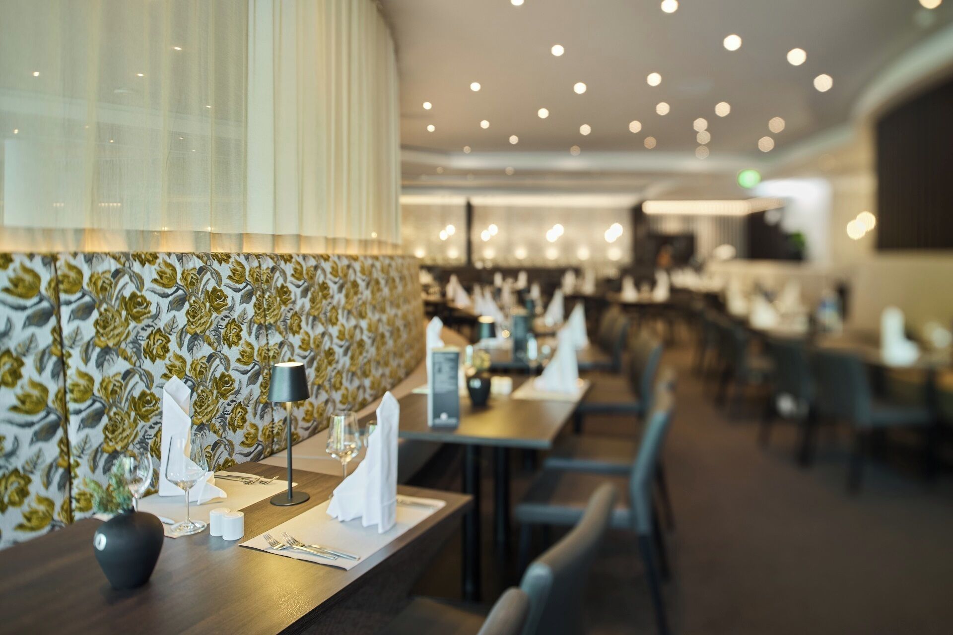 Interno di un ristorante con tavoli apparecchiati, una parete decorata e un soffitto con faretti.