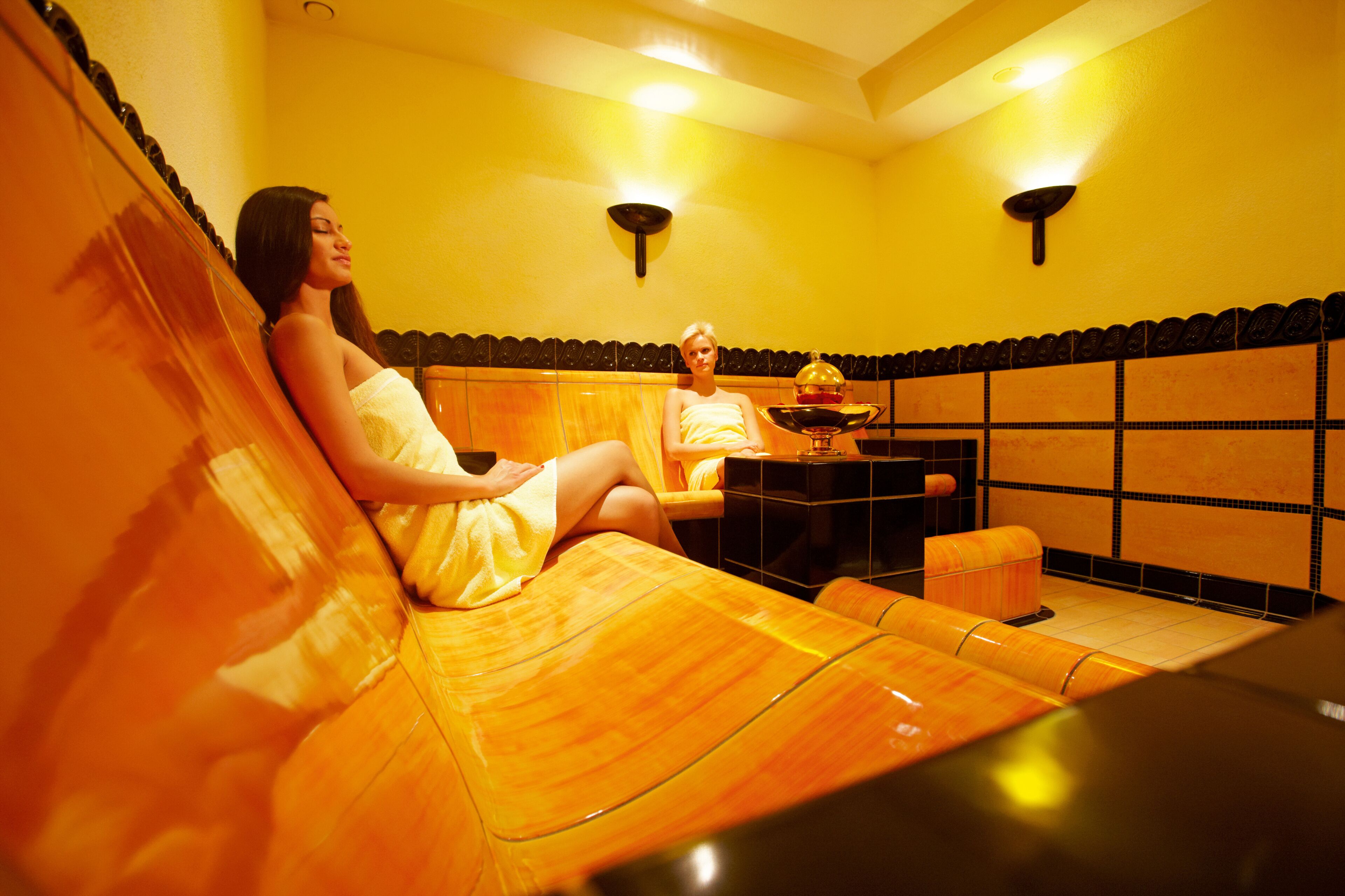 A sauna with two wooden benches, a small table with a bowl, and wall-mounted lights.