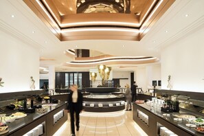 Un vestíbul d'hotel modern amb una recepció central, una zona de buffet i un sostre alt amb il·luminació empotrada.