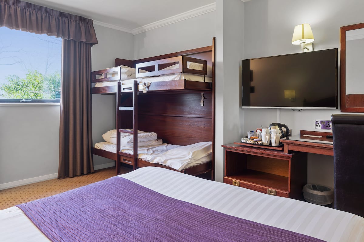A hotel room with a bunk bed, a desk with a lamp, a television, and a window with curtains.