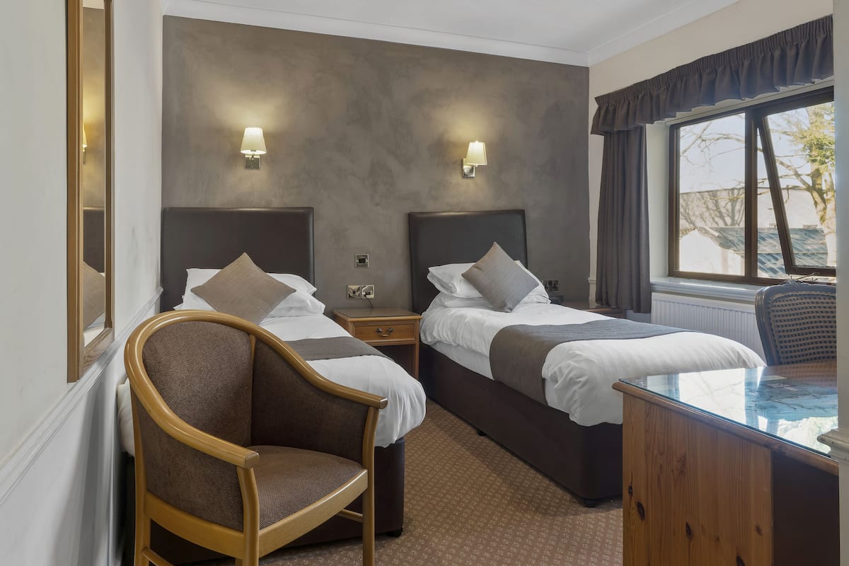 A hotel room with two beds, a wooden chair, a desk, and a window with curtains.