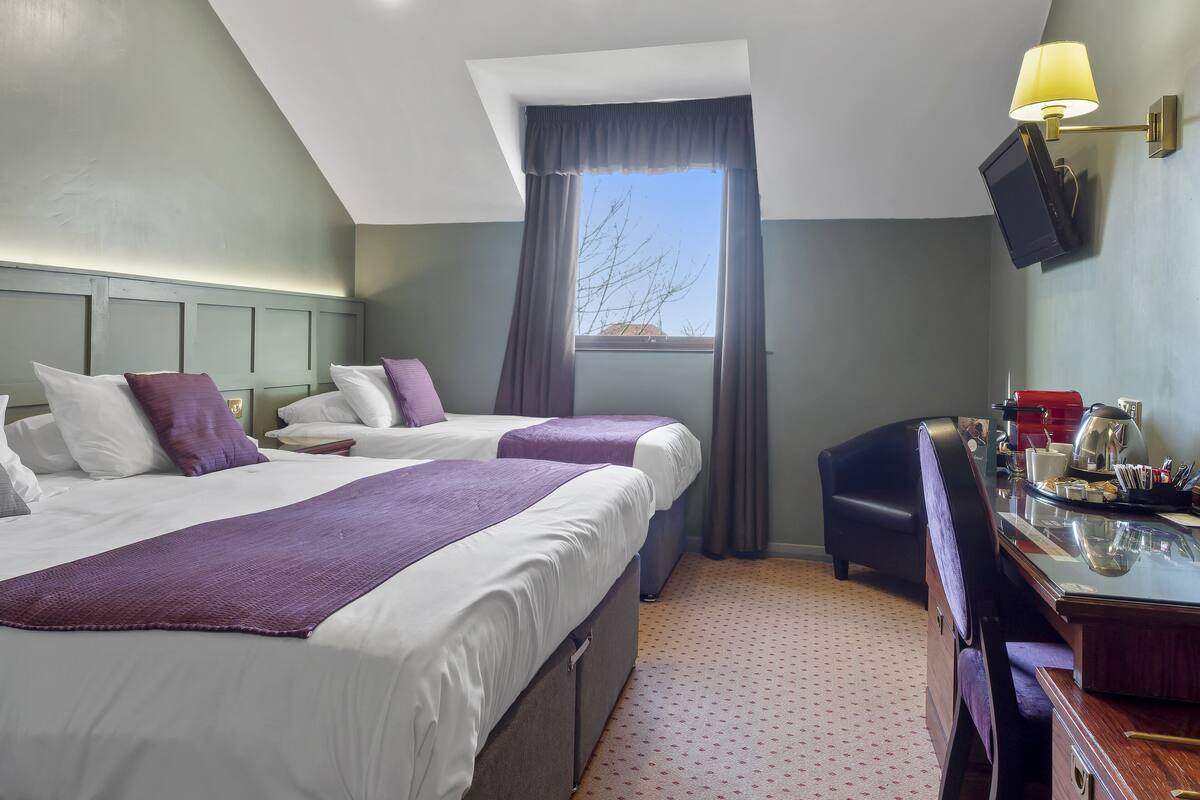 A hotel room with two beds, a desk, a television, and a window with curtains.