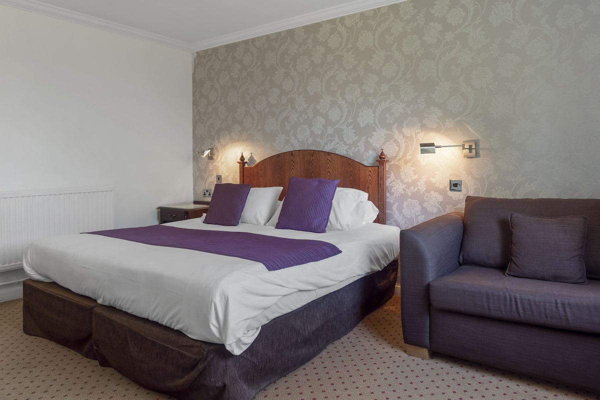 A neatly arranged bedroom with a large bed, a nightstand, a dresser, and a sofa.