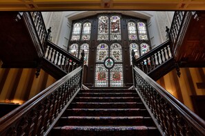 Un magnifique escalier, orné de balustrades travaillées et surmonté d’une fenêtre à vitraux.
