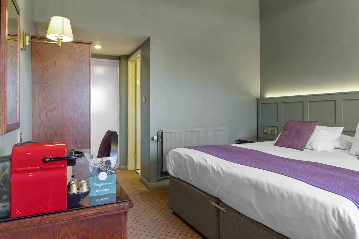 A hotel room with a bed, a red coffee machine, a wooden dresser, and a door leading to another room.