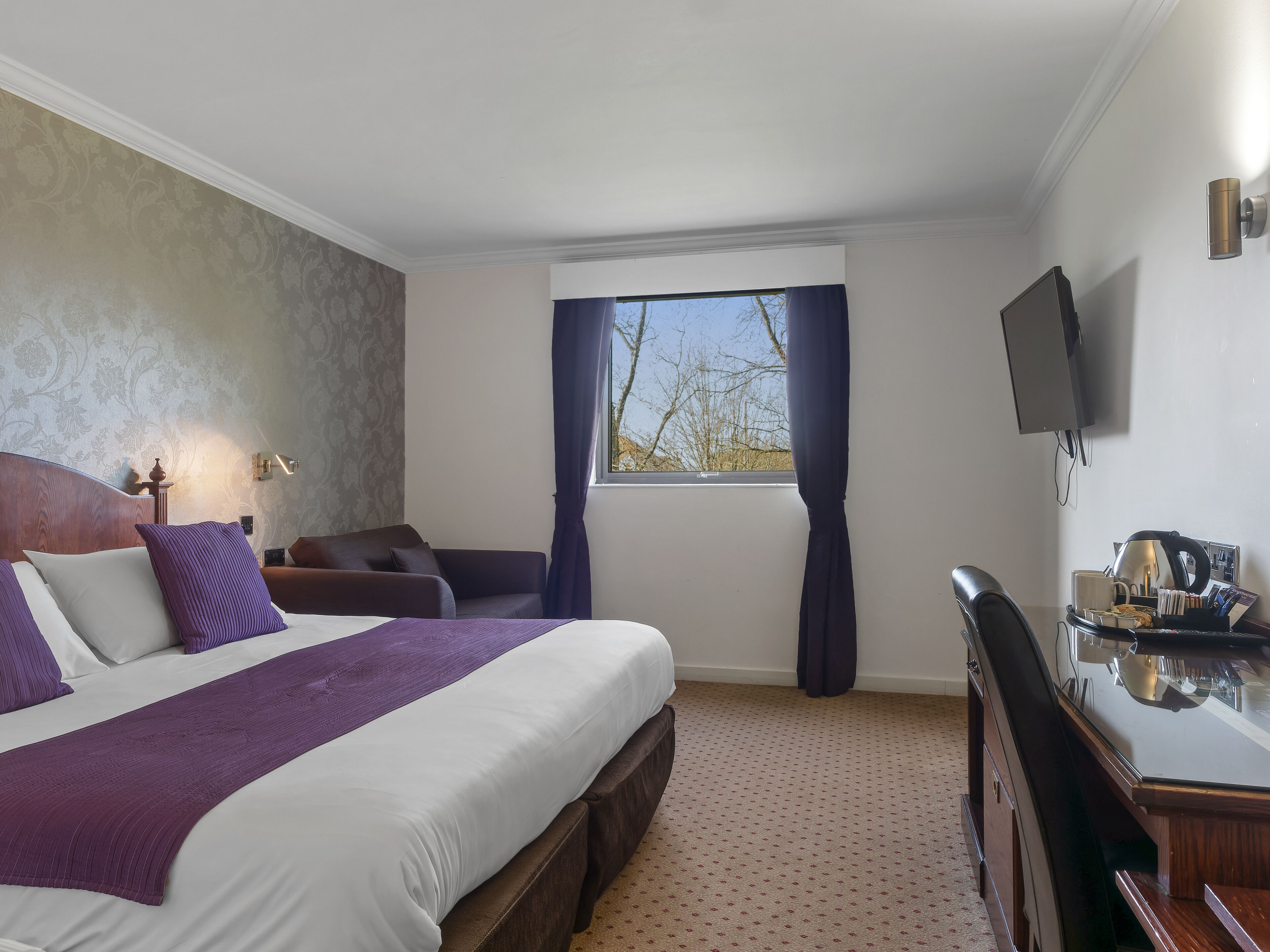 A hotel room with a large bed, a desk, a chair, a television, and a window with curtains.