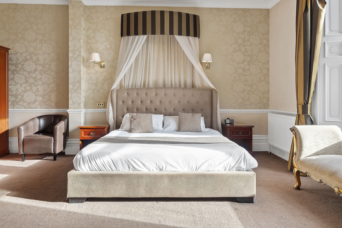 A large bed with a canopy, two bedside tables, a chair, and a lamp.