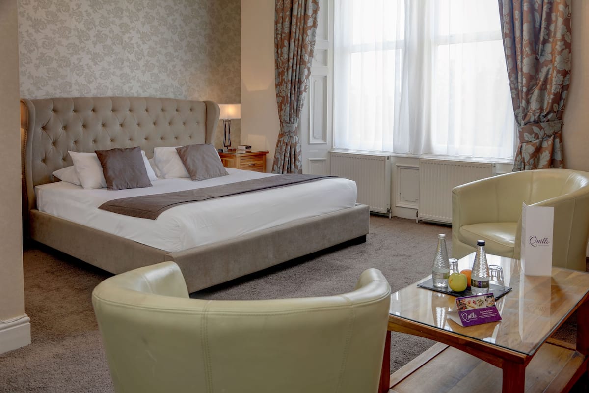 A hotel room with a large bed, a glass coffee table, a chair, and a view of the outdoors.