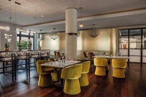 Zona pranzo moderna con pavimento in legno, sedie imbottite gialle e un tavolo centrale con bicchieri.