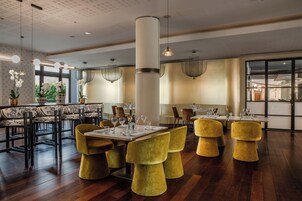 Un comedor moderno con suelo de madera, sillas tapizadas en amarillo y una mesa central con cristalería.