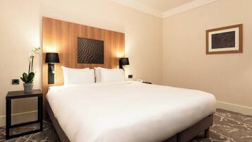 A hotel room with a large bed, two bedside tables, a wall-mounted TV, and a framed picture.
