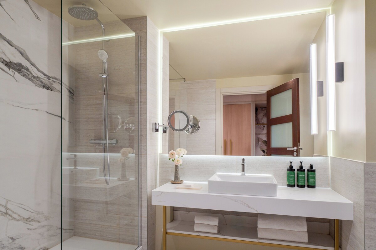 Een moderne badkamer met een douchecabine van glas, een wastafel van wit marmer en een spiegel met geïntegreerde verlichting.