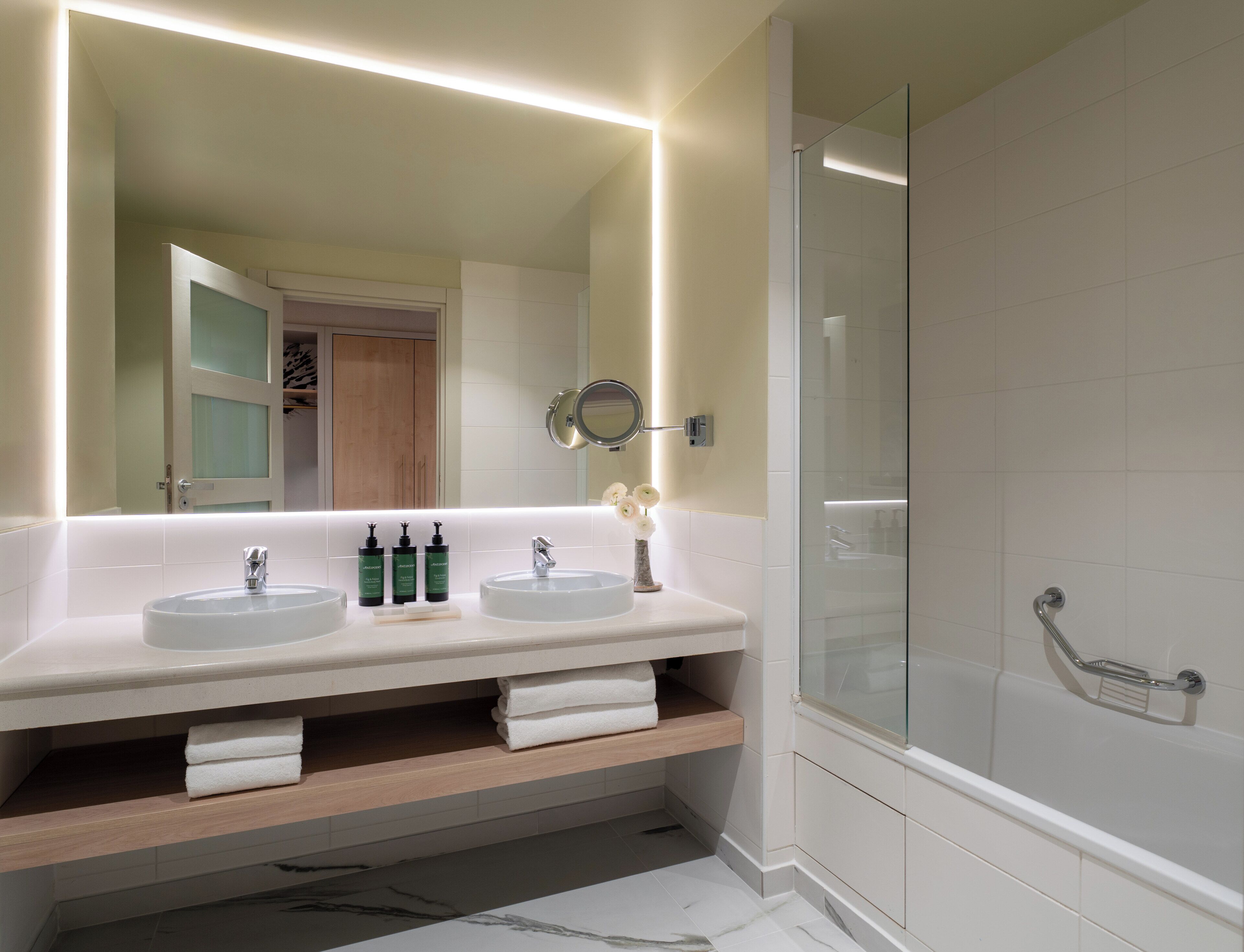 A modern bathroom with two sinks, a glass shower enclosure, and a mirror with integrated lighting.