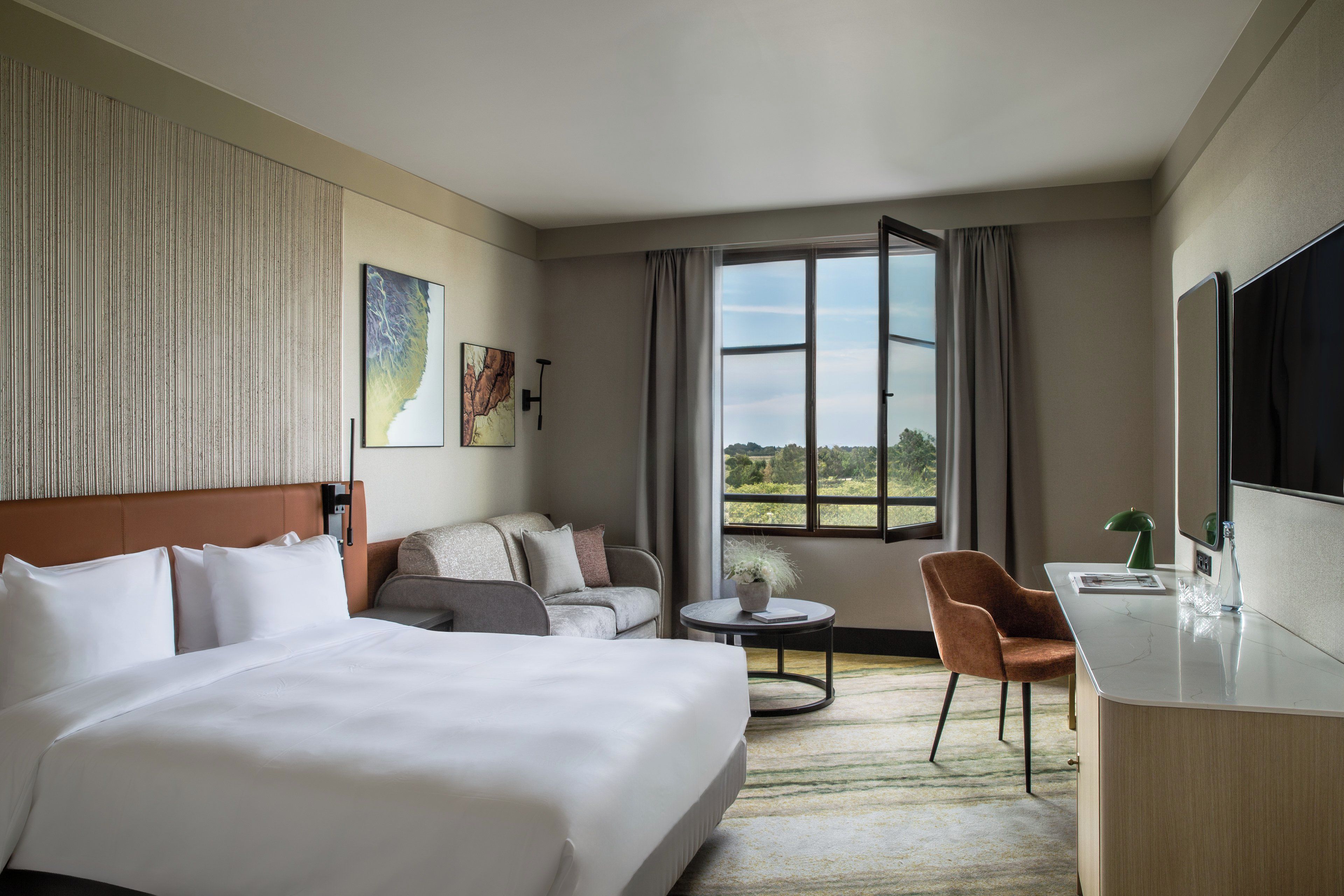 A hotel room with a large bed, a sofa, a desk, and a view of the outdoors.
