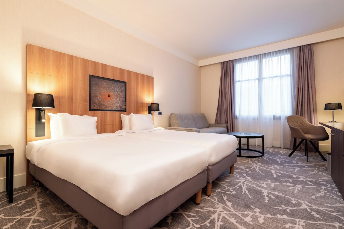 Een hotelkamer met een groot bed, twee nachtkastjes met lampen, een sofa, een kleine ronde tafel en een stoel.