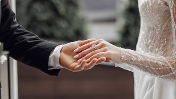A close-up of a hand holding another hand, with a wedding ring visible.