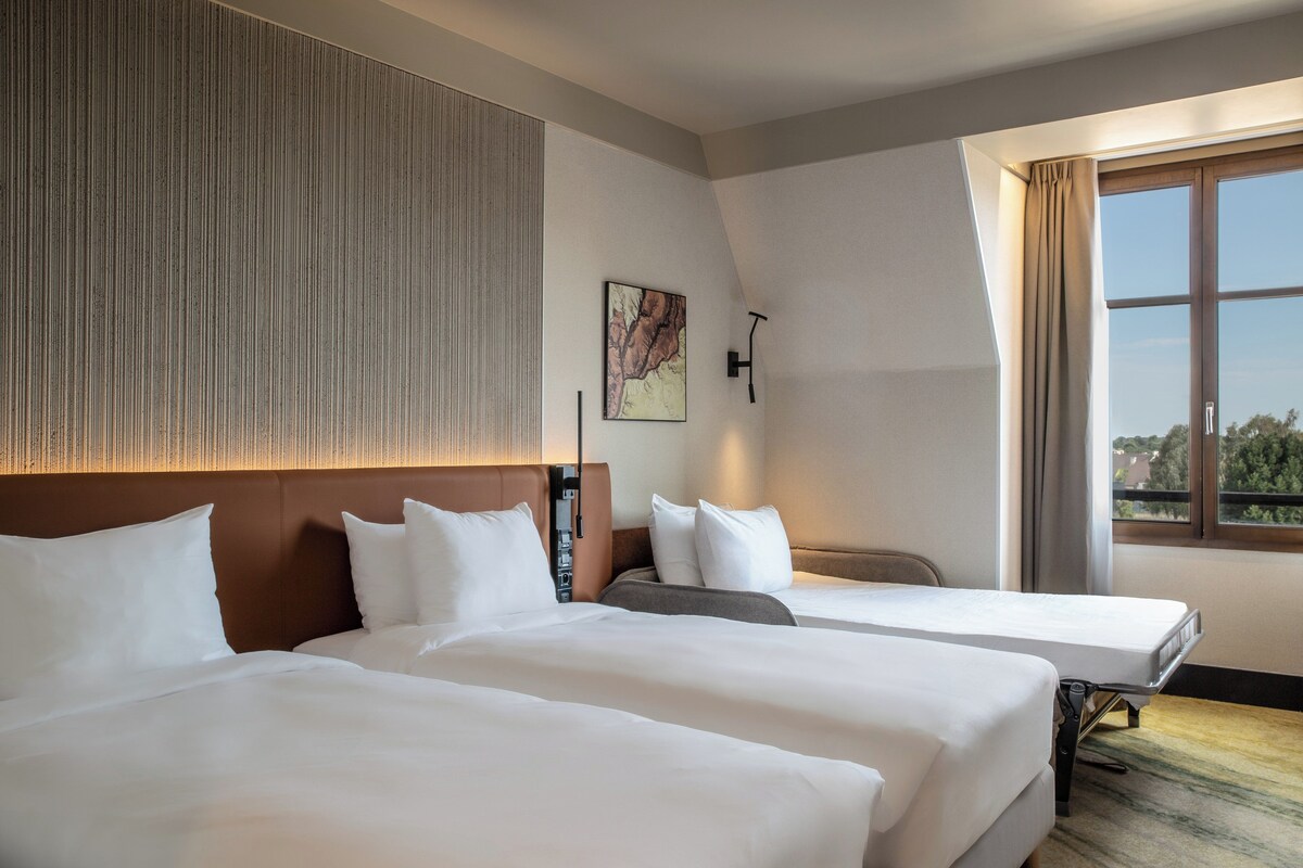 Une chambre d’hôtel avec deux lits, une grande fenêtre et une œuvre d’art accrochée au mur.