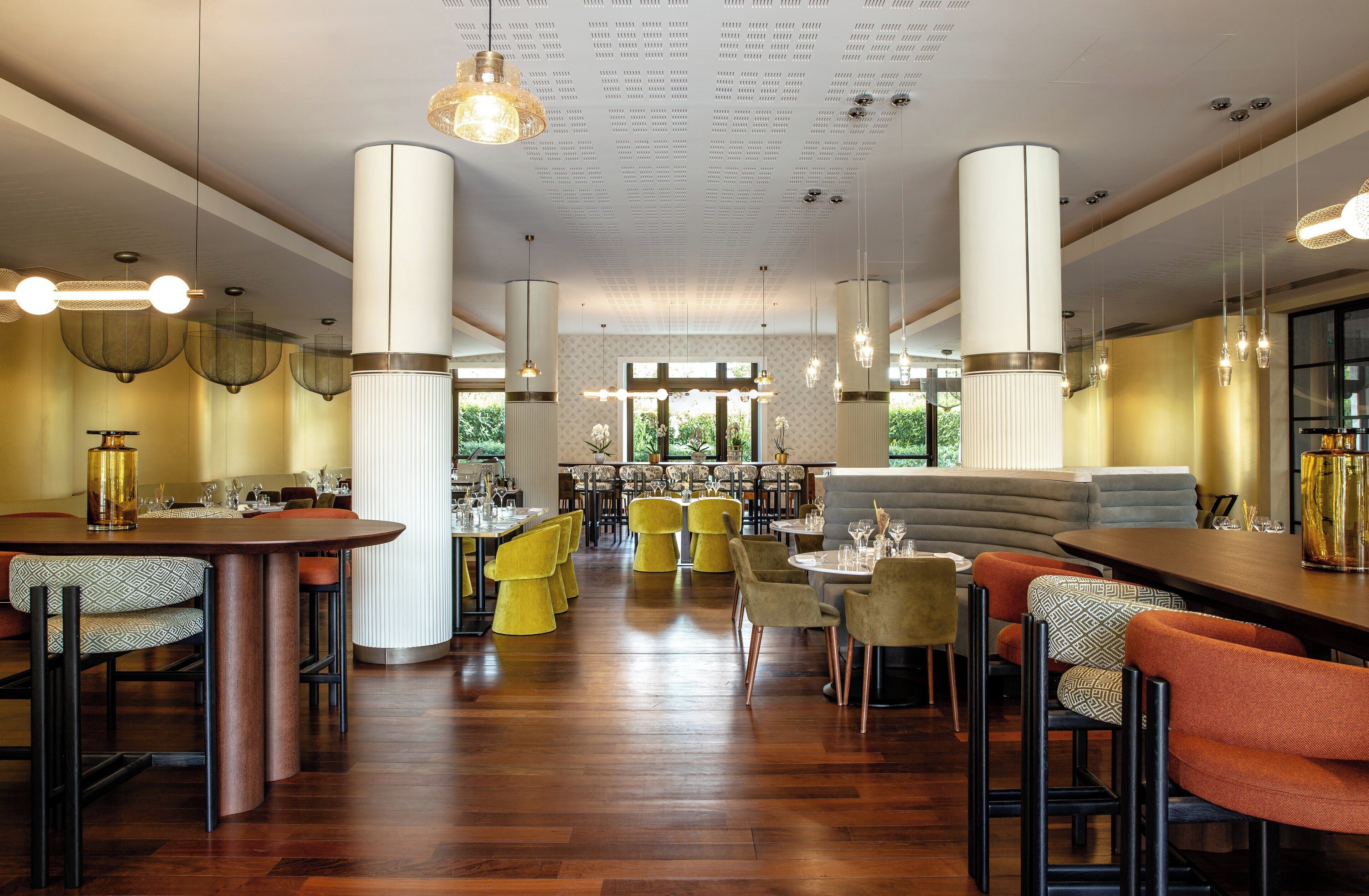 Un restaurant spacieux avec de hauts plafonds, plusieurs espaces de restauration et une variété de styles de tables et de chaises.