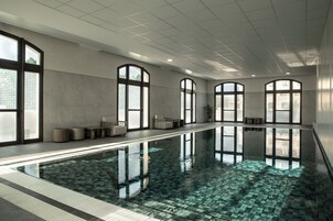 Una amplia piscina interior con agua cristalina, rodeada de zonas de estar y grandes ventanales.