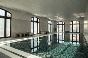 A large indoor swimming pool with clear water, surrounded by seating areas and large windows.
