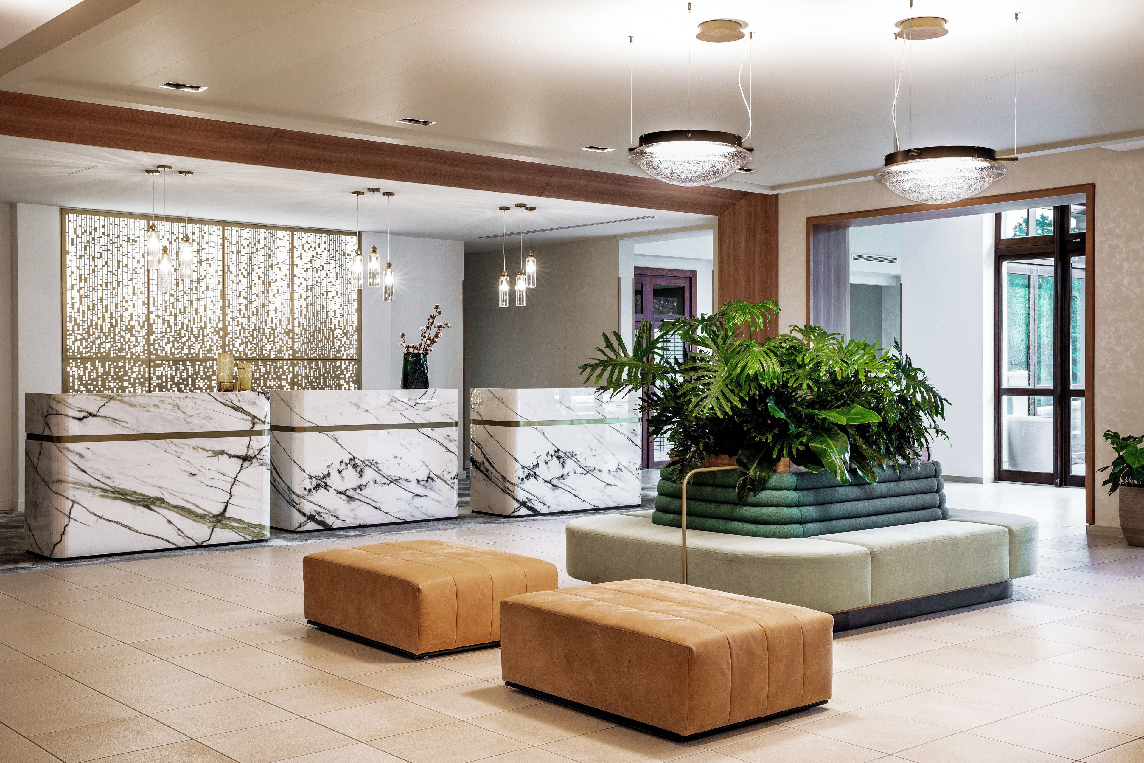 A modern lobby with marble reception counters, a large plant centerpiece, and a seating area with ottomans.