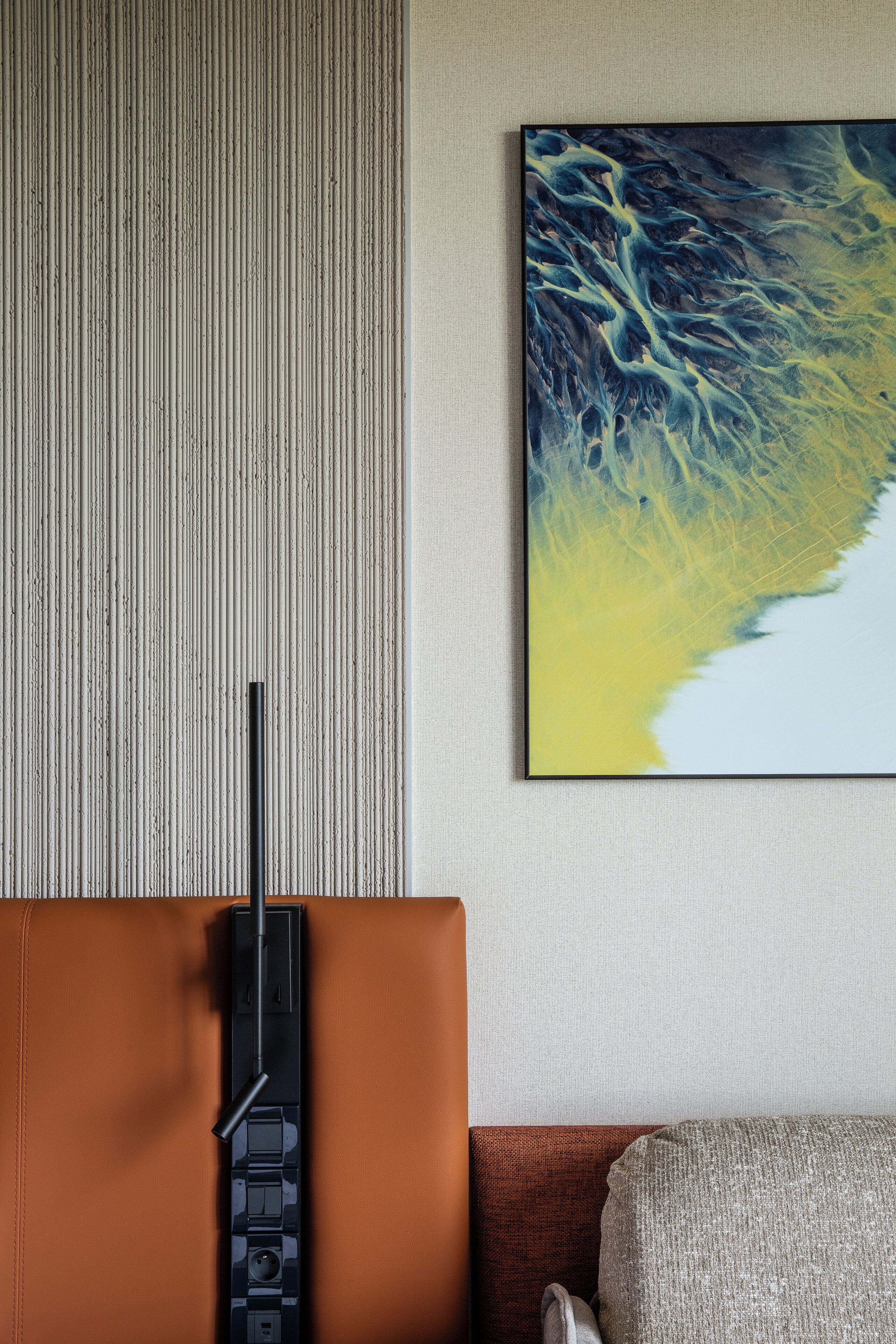 A room with a textured wall, a mounted painting, a brown leather sofa, and a black standing lamp.